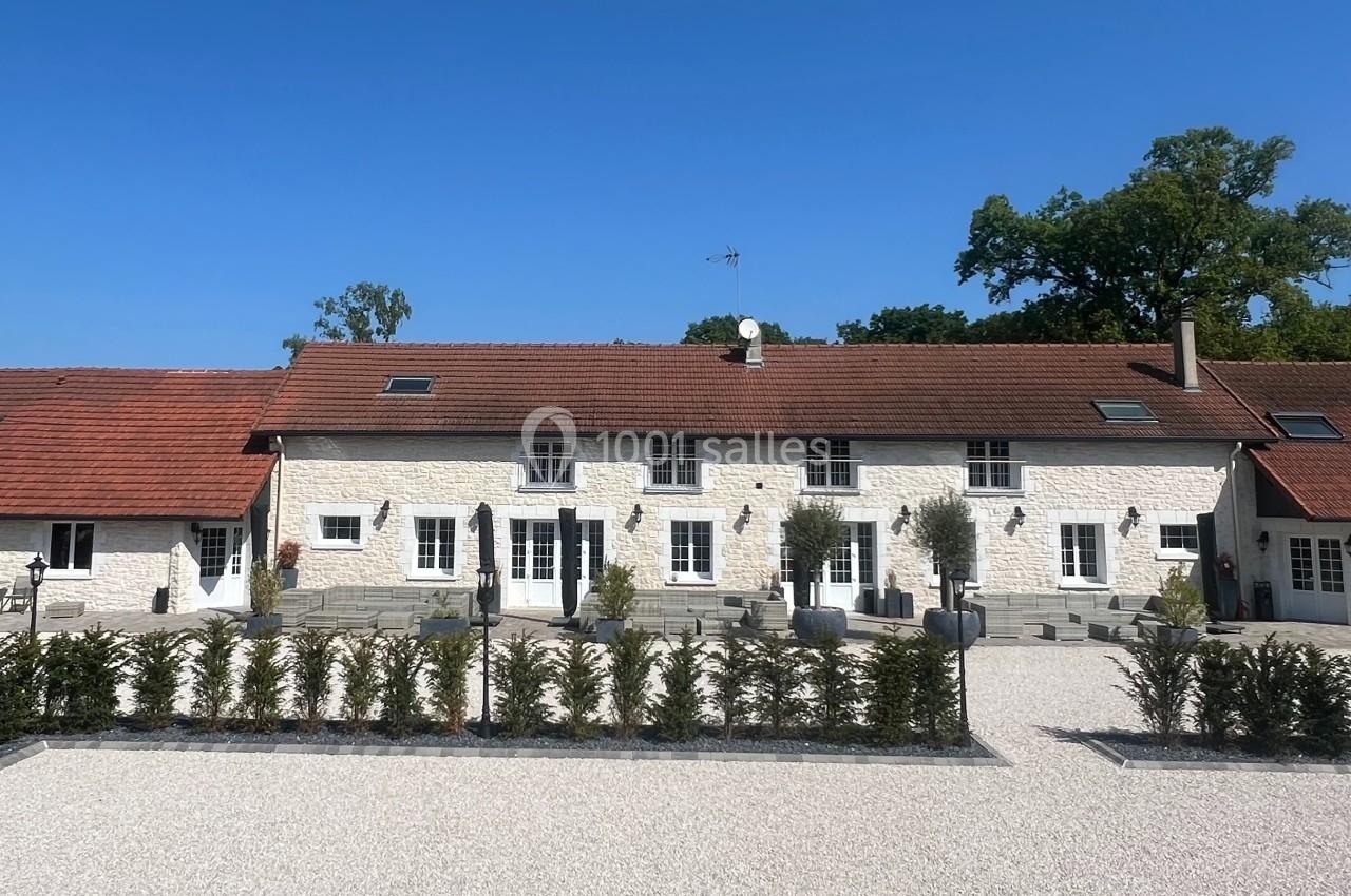 Grande maison en pierre blanche avec toit en tuiles rouges, entourée d'une cour gravillonnée et de haies taillées.