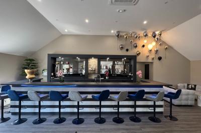 Balancelle en bois rustique sur une pelouse artificielle, avec des bâtiments en pierre et un ciel dégagé en arrière-plan.