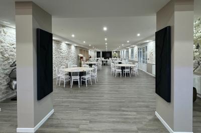 Balancelle en bois rustique sur une pelouse artificielle, avec des bâtiments en pierre et un ciel dégagé en arrière-plan.