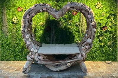 Balancelle en bois rustique sur une pelouse artificielle, avec des bâtiments en pierre et un ciel dégagé en arrière-plan.