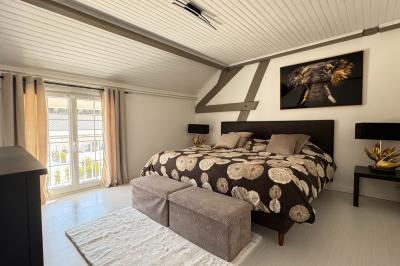 Balancelle en bois rustique sur une pelouse artificielle, avec des bâtiments en pierre et un ciel dégagé en arrière-plan.