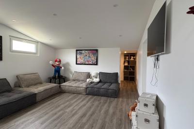 Balancelle en bois rustique sur une pelouse artificielle, avec des bâtiments en pierre et un ciel dégagé en arrière-plan.