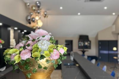 Balancelle en bois rustique sur une pelouse artificielle, avec des bâtiments en pierre et un ciel dégagé en arrière-plan.