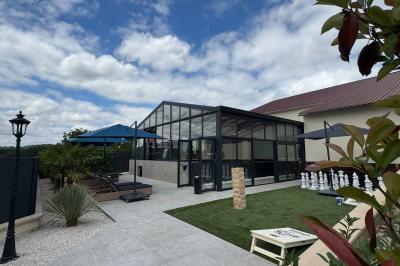 Balancelle en bois rustique sur une pelouse artificielle, avec des bâtiments en pierre et un ciel dégagé en arrière-plan.