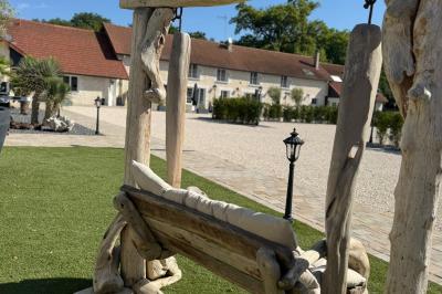 Balancelle en bois rustique sur une pelouse artificielle, avec des bâtiments en pierre et un ciel dégagé en arrière-plan.