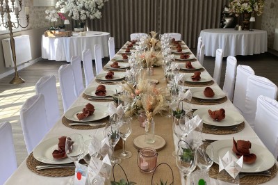 Grande table décorée pour un repas festif, avec nappes en toile de jute, serviettes pliées et centres de table fleuris.