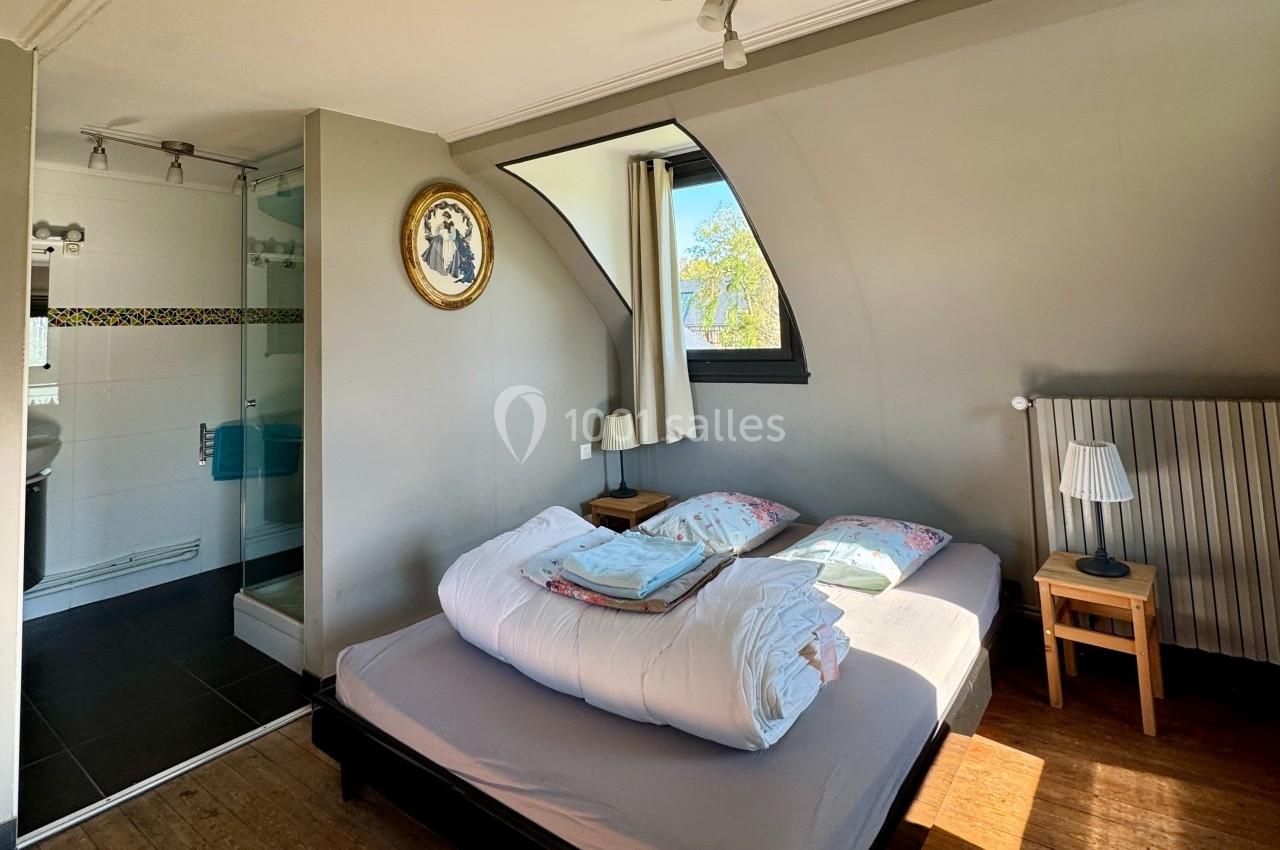 Chambre lumineuse avec lit double, salle de bain attenante, fenêtre en arc et décoration murale.