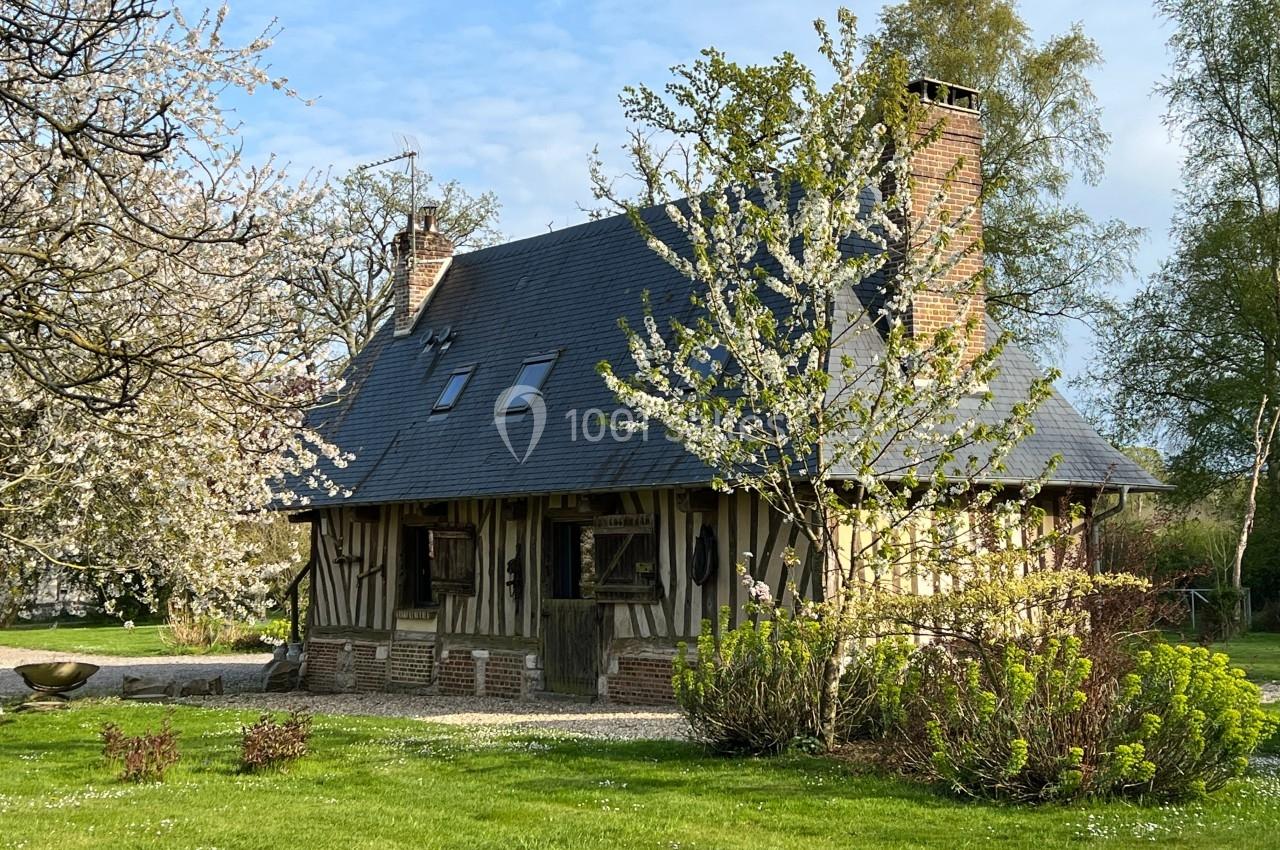 Maison à colombages traditionnelle entourée d'arbres en fleurs et d'un jardin verdoyant sous un ciel clair.