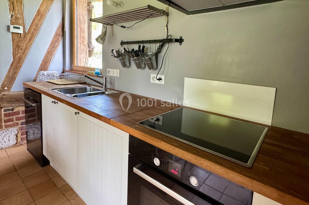 Cuisine moderne avec plan de travail en bois, évier double, plaques de cuisson et ustensiles suspendus.