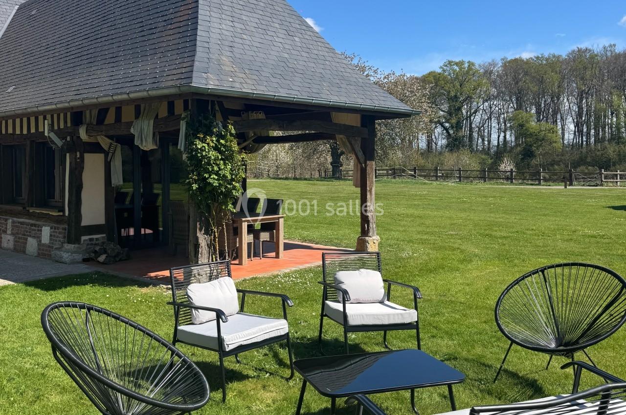 Terrasse avec mobilier de jardin devant une maison à colombages, entourée d'une pelouse et d'arbres.