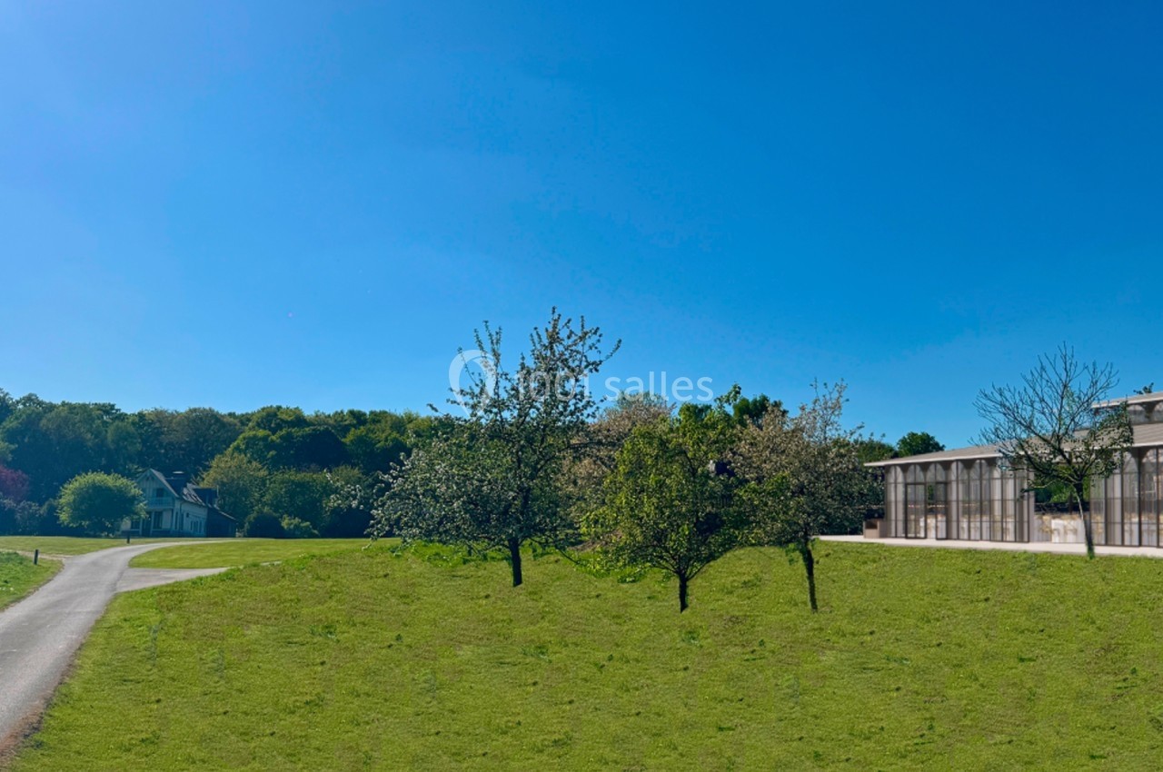 Pelouse verdoyante avec quelques arbres, une serre vitrée à droite et un chemin menant à une petite maison à gauche.