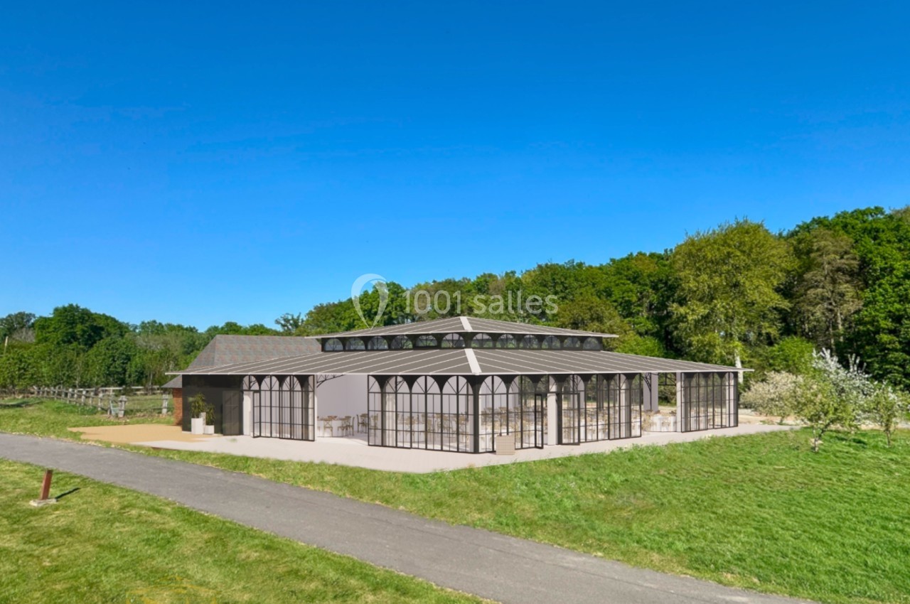 Serre moderne en verre et métal entourée de verdure, avec un chemin en premier plan et une forêt en arrière-plan.