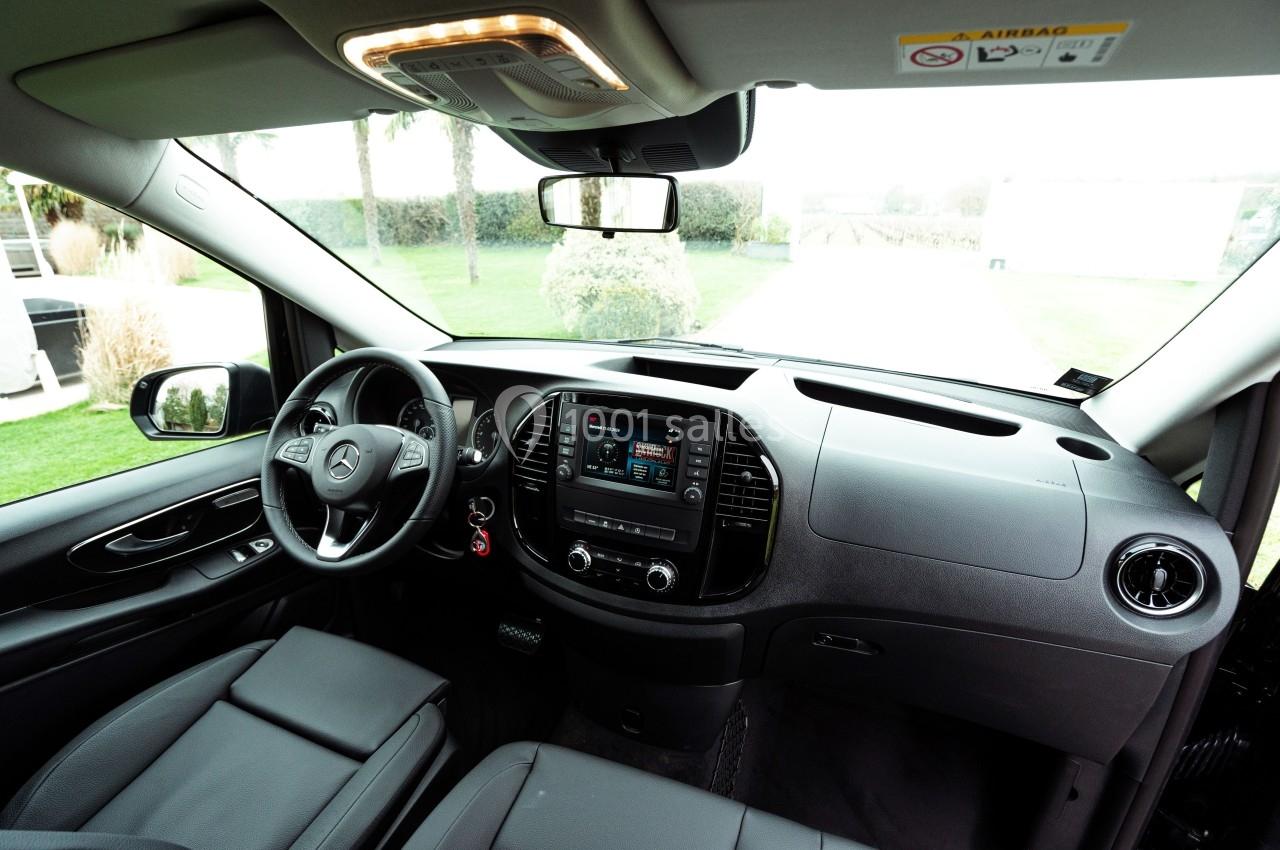 Intérieur d'un véhicule avec volant, tableau de bord numérique et sièges en cuir noir, vue depuis l'avant.