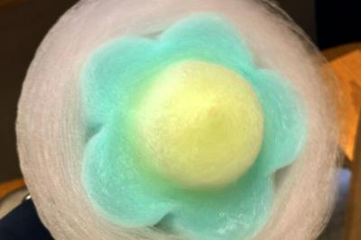 Vue de dessus d'une barbe à papa rose tenue par une personne portant un t-shirt noir avec un logo blanc.