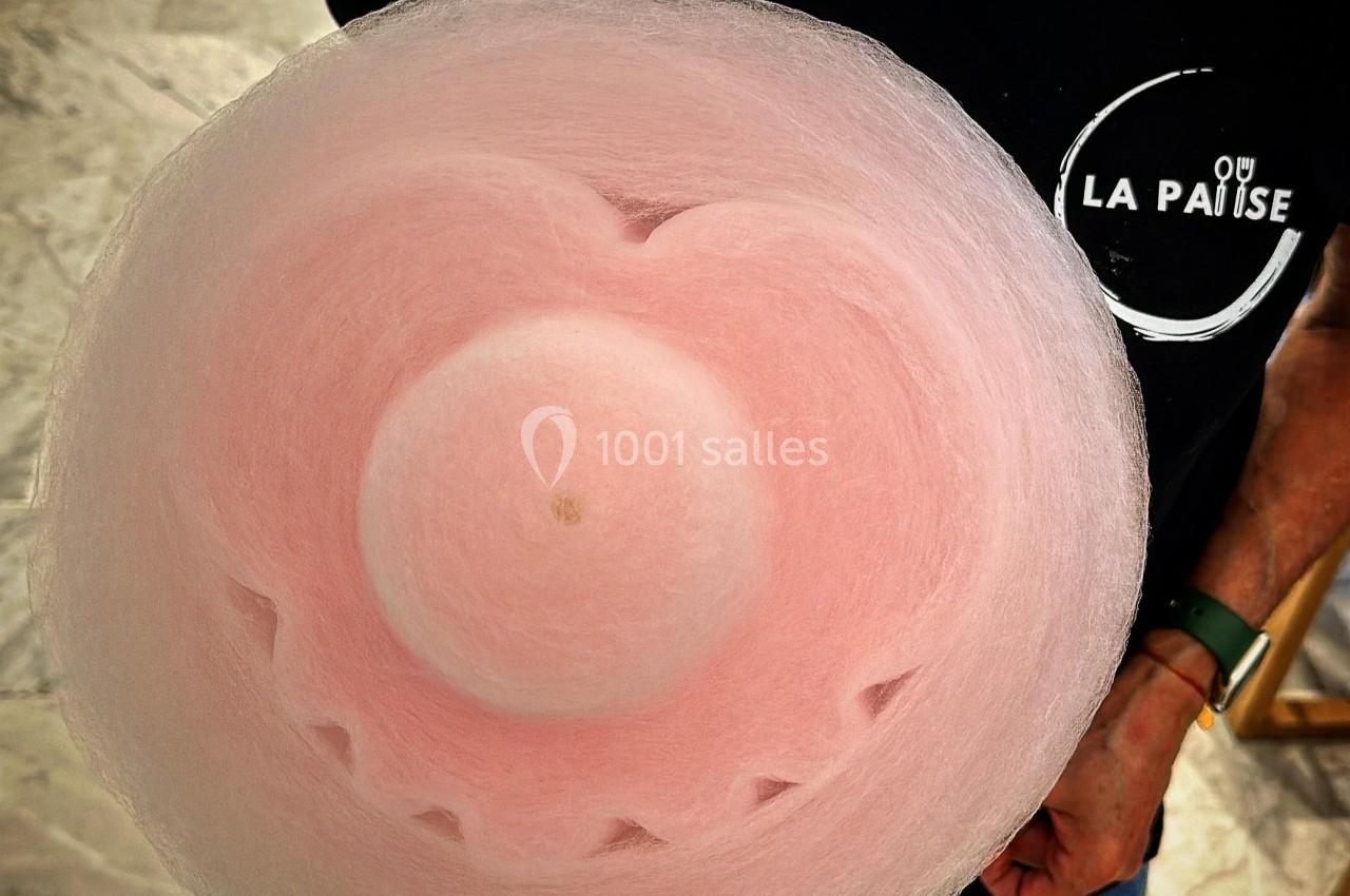 Vue de dessus d'une barbe à papa rose tenue par une personne portant un t-shirt noir avec un logo blanc.