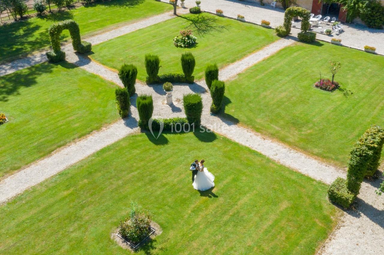 Vue aérienne d'un jardin symétrique avec des allées gravillonnées, des haies taillées et un couple marchant au centre.
