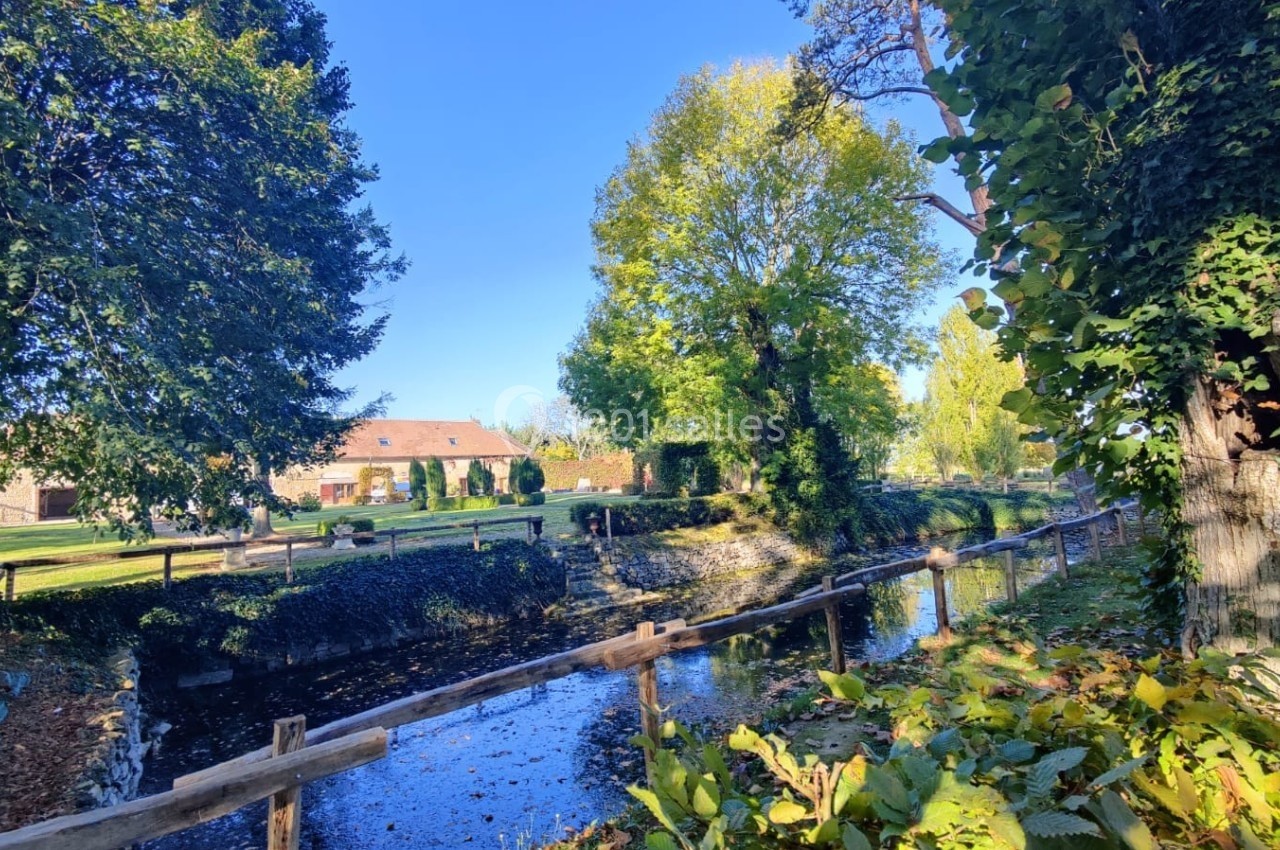 Un petit canal bordé d'arbres et de végétation, avec des maisons en arrière-plan sous un ciel bleu.