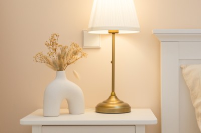 Panier en osier posé au sol devant un grand miroir, avec un lit et une lampe en arrière-plan dans une chambre.