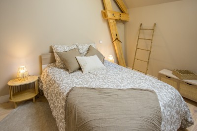 Panier en osier posé au sol devant un grand miroir, avec un lit et une lampe en arrière-plan dans une chambre.