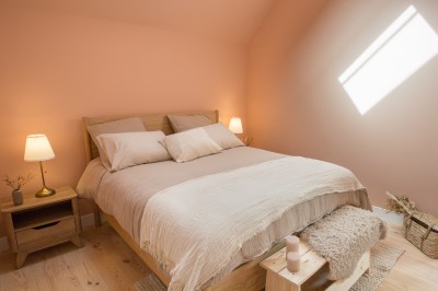 Panier en osier posé au sol devant un grand miroir, avec un lit et une lampe en arrière-plan dans une chambre.