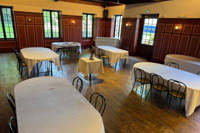 Salle avec des tables rondes et rectangulaires recouvertes de nappes blanches, entourées de chaises noires.
