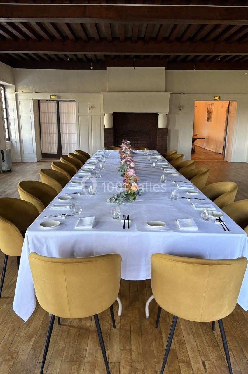 Table dressée avec une nappe blanche, vaisselle et décoration florale, entourée de chaises jaunes dans une salle lumineuse.