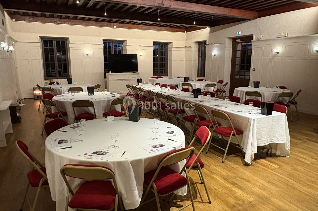 Salle de réception avec tables rondes dressées, chaises rouges et éclairage chaleureux.