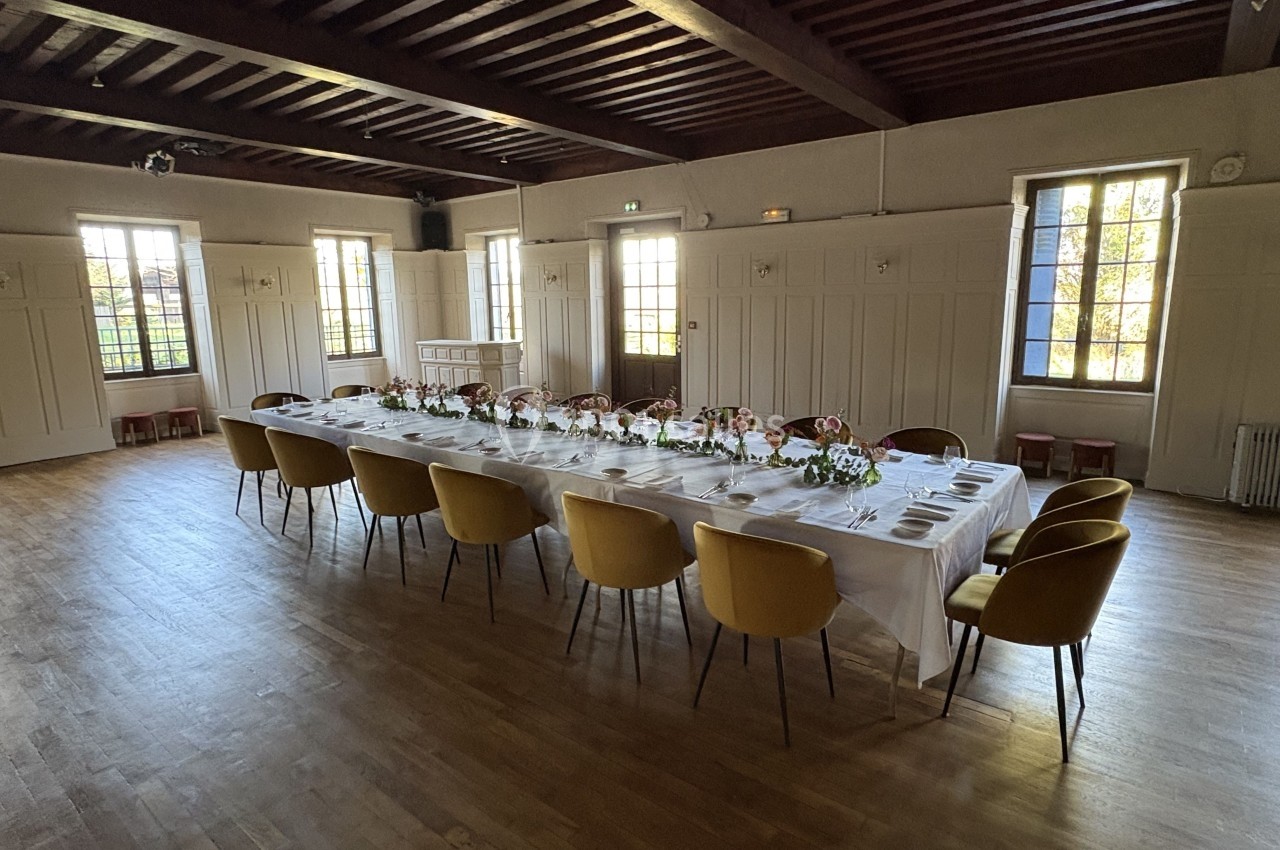 Table rectangulaire élégamment dressée avec des fleurs et des chaises jaunes, dans une salle lumineuse au parquet en bois.