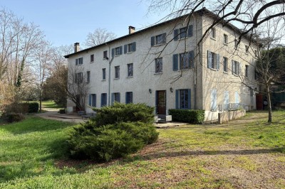 Grande maison blanche à deux étages avec volets bleus, entourée d'arbres et d'un jardin verdoyant.