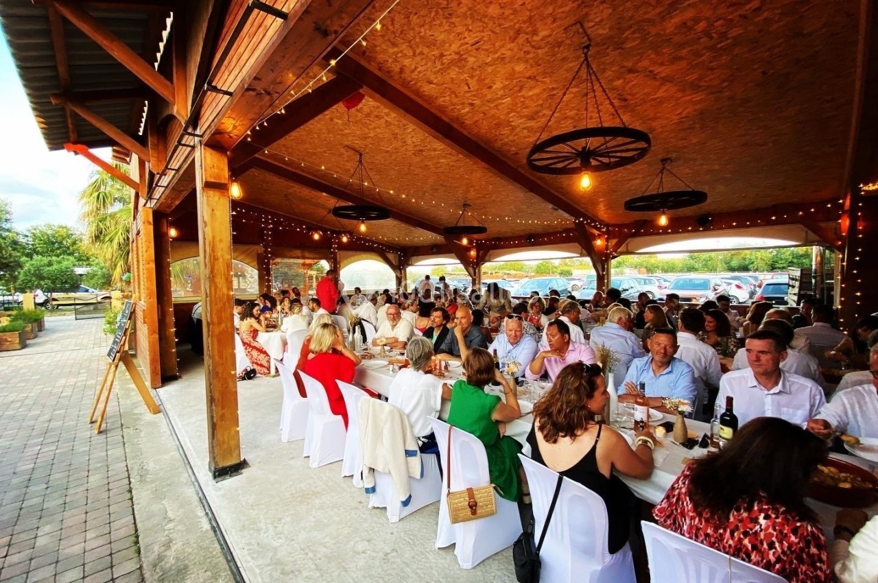 Des convives assis à des tables décorées sous une grande structure en bois lors d'un événement festif en extérieur.