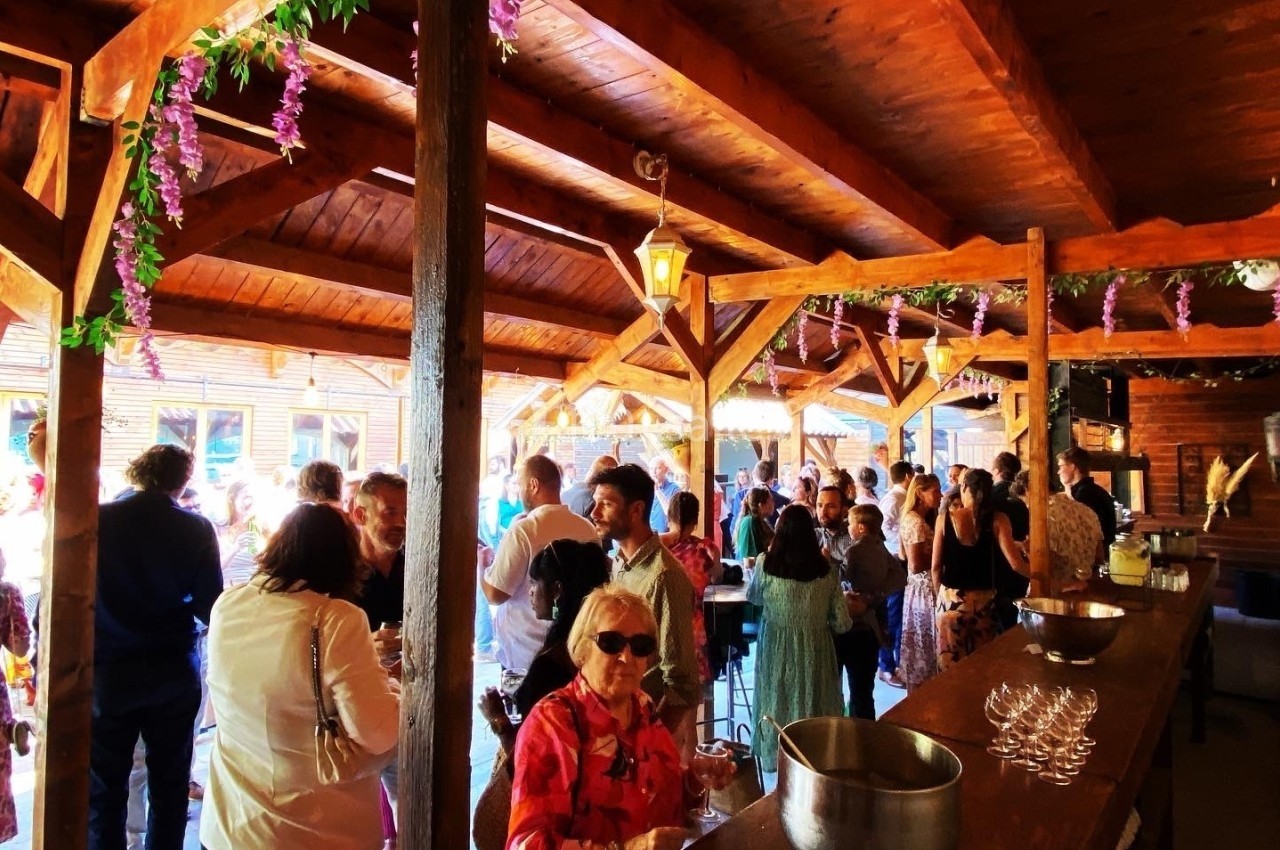 Groupe de personnes rassemblées dans un espace en bois décoré de fleurs violettes, lors d'un événement convivial.