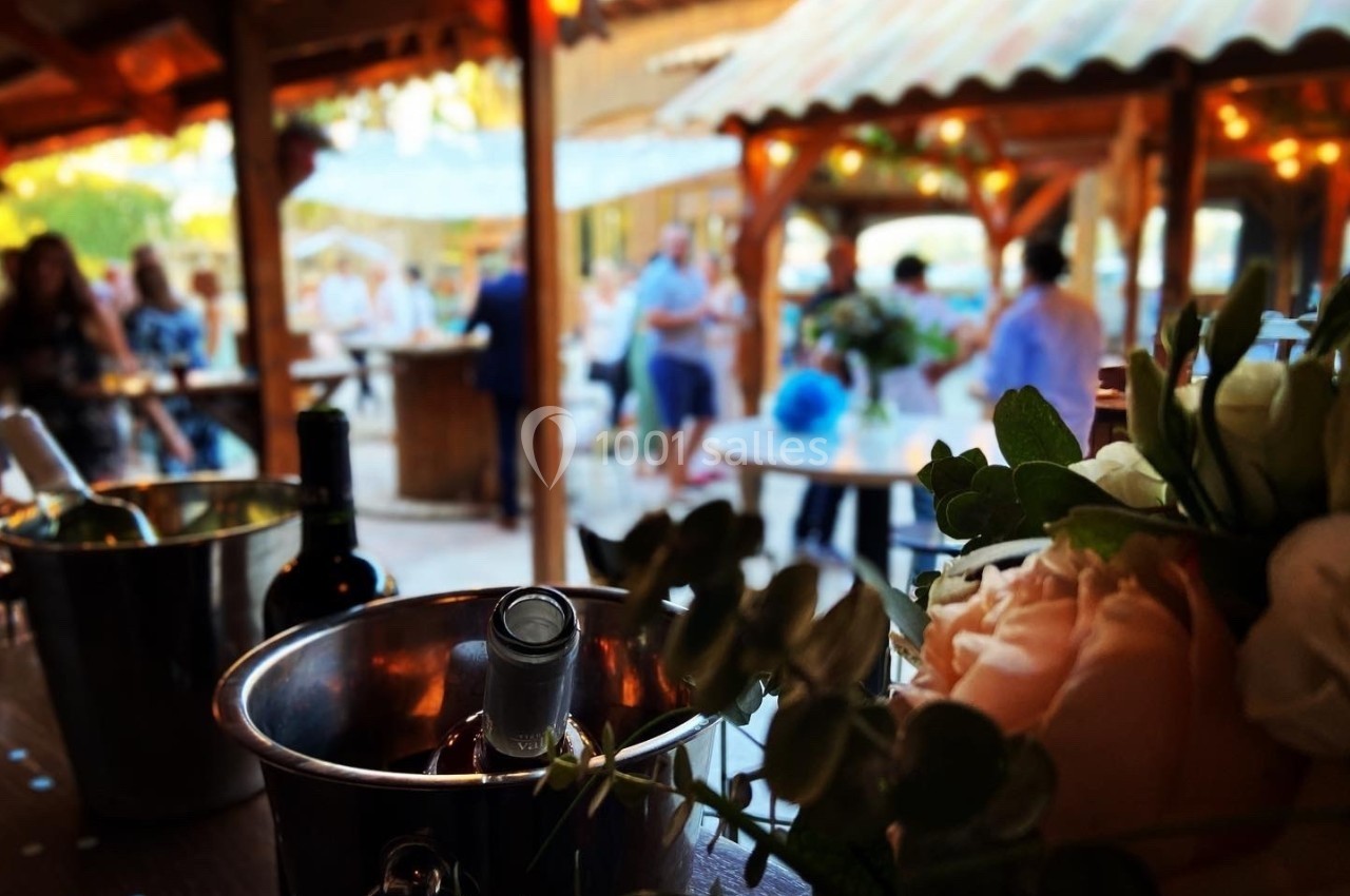 Des tables décorées et des invités flous en arrière-plan sous une pergola, avec un seau à glace et des fleurs au premier…