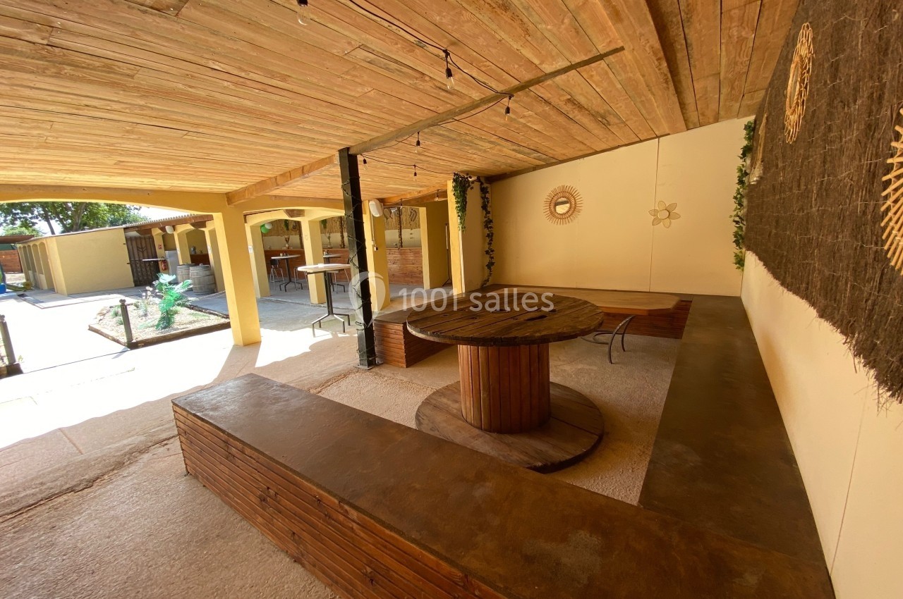 Espace extérieur couvert avec table ronde en bois, bancs intégrés et décorations murales naturelles.