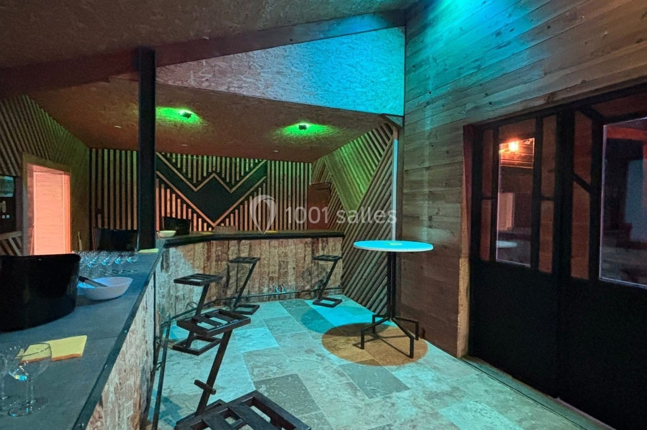 Intérieur d'un bar avec comptoir en bois, tabourets hauts, éclairage coloré et murs décorés de motifs géométriques.