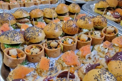 Plateaux garnis de bouchées variées, incluant mini-burgers, canapés au saumon et amuse-bouches garnis de graines.