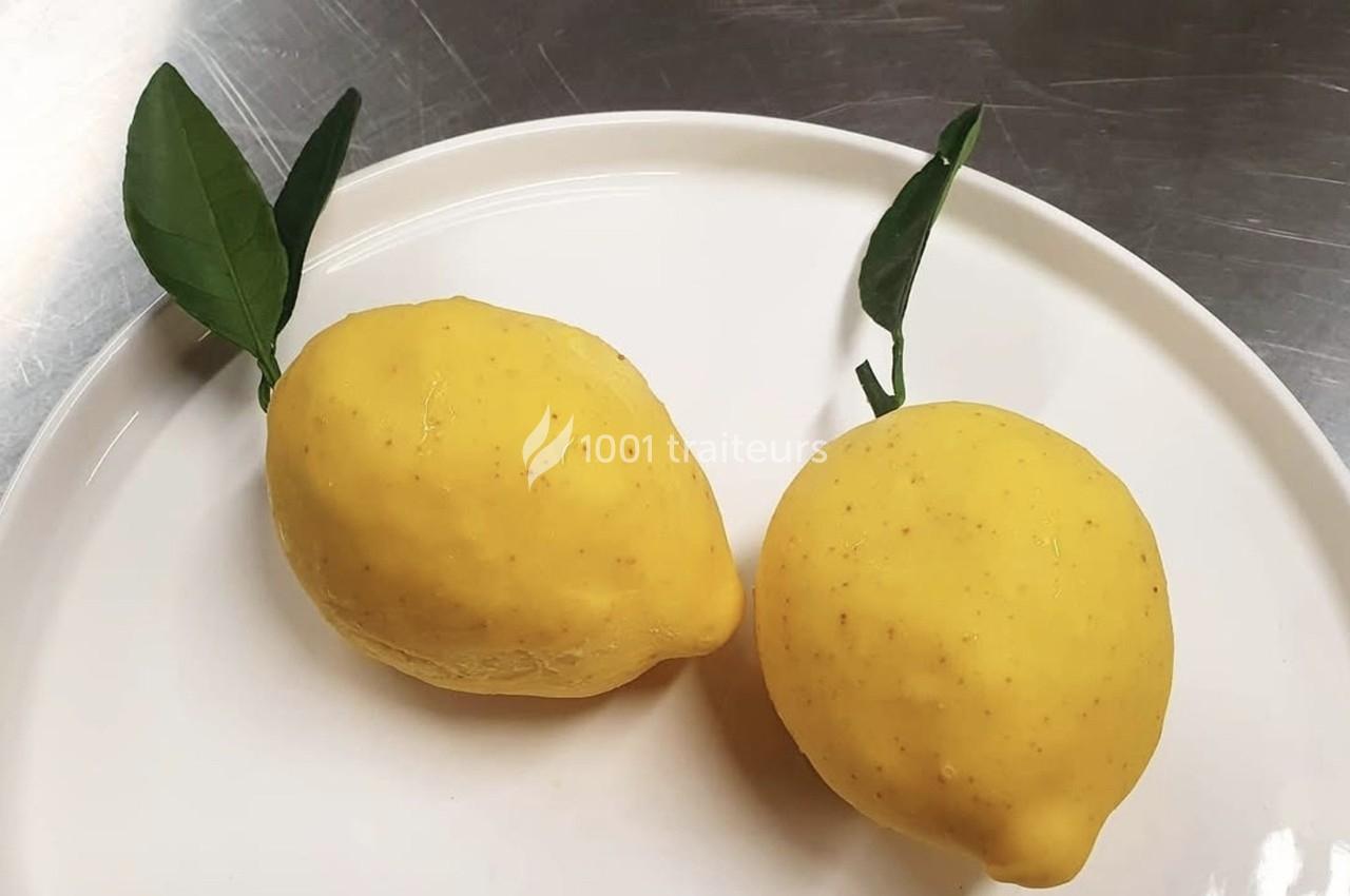 Deux citrons jaunes avec leurs feuilles posés sur une assiette blanche, sur une surface métallique.