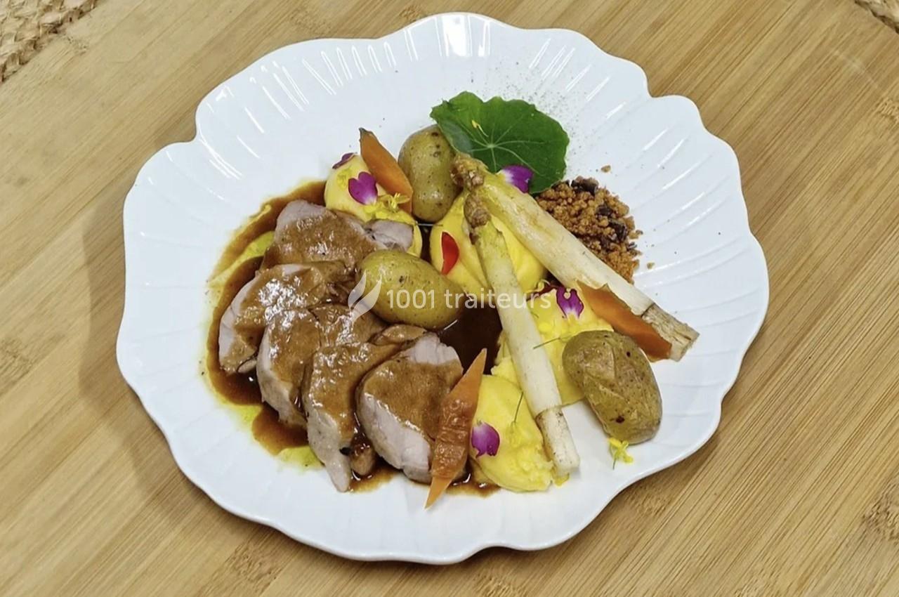 Assiette de viande tranchée avec sauce, pommes de terre, asperges, purée et décorations florales sur une assiette blanche.
