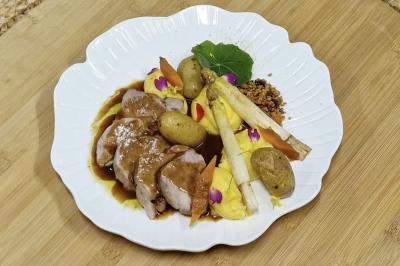 Assiette de viande tranchée avec sauce, pommes de terre, asperges, purée et décorations florales sur une assiette blanche.