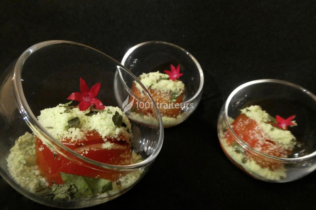 Trois verrines contenant une préparation à base de tomate, herbes fraîches, poudre verte et fleurs rouges décoratives.