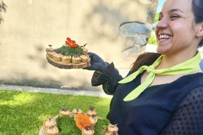 Miniature Traiteur Nousty (Pyrénées-Atlantiques) - Adquat Traiteur #22 Femme souriante cueillant des baies dans un jardin sous un parapluie par temps nuageux.