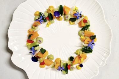 Miniature Traiteur Nousty (Pyrénées-Atlantiques) - Adquat Traiteur #3 Femme souriante cueillant des baies dans un jardin sous un parapluie par temps nuageux.