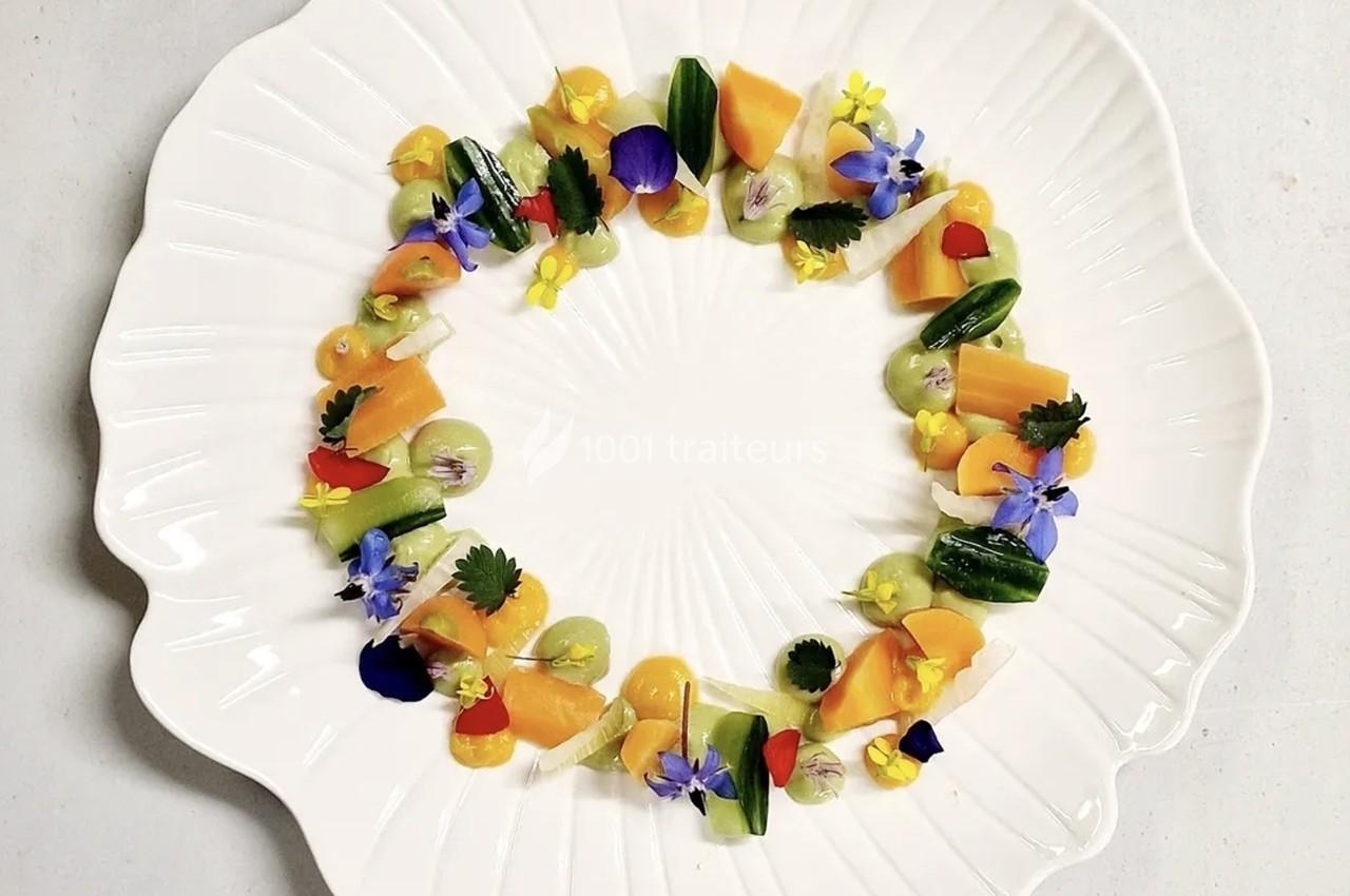 Assiette blanche décorée de légumes colorés, fleurs comestibles et herbes disposés en cercle.