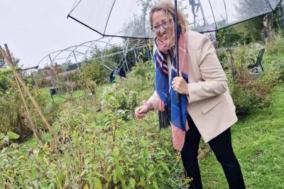 Miniature Traiteur Nousty (Pyrénées-Atlantiques) - Adquat Traiteur #23 Femme souriante cueillant des baies dans un jardin sous un parapluie par temps nuageux.