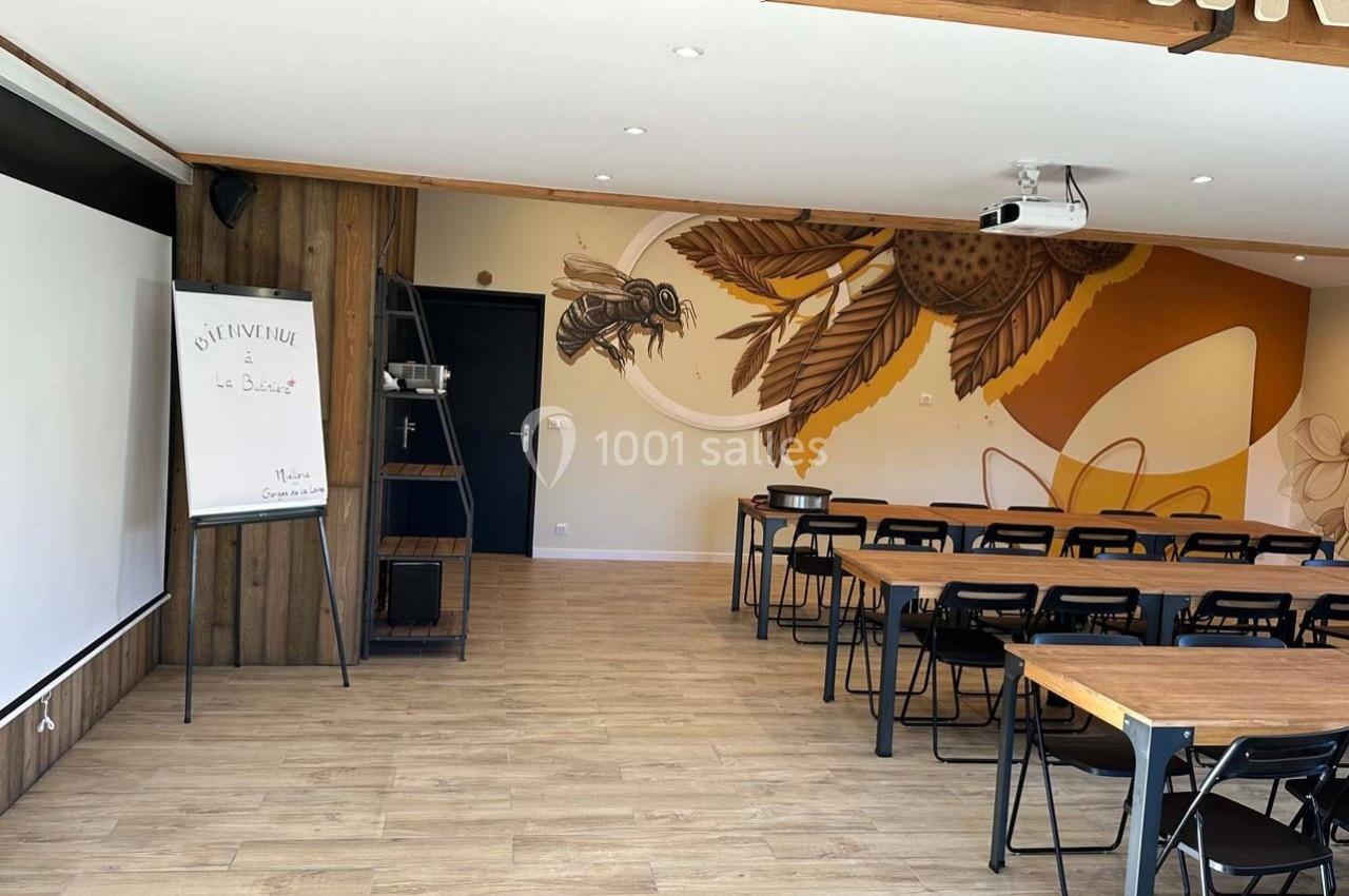 Salle de réunion lumineuse avec tables en bois, chaises noires, tableau blanc et fresque murale décorative.
