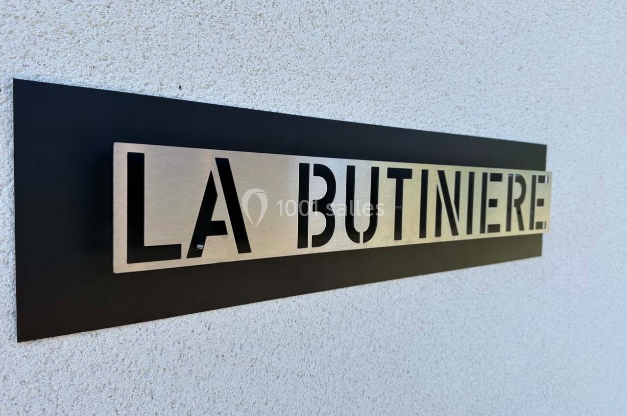 Plaque murale en métal avec l'inscription ’LA BUTINIERE’ sur fond noir fixée sur un mur clair.