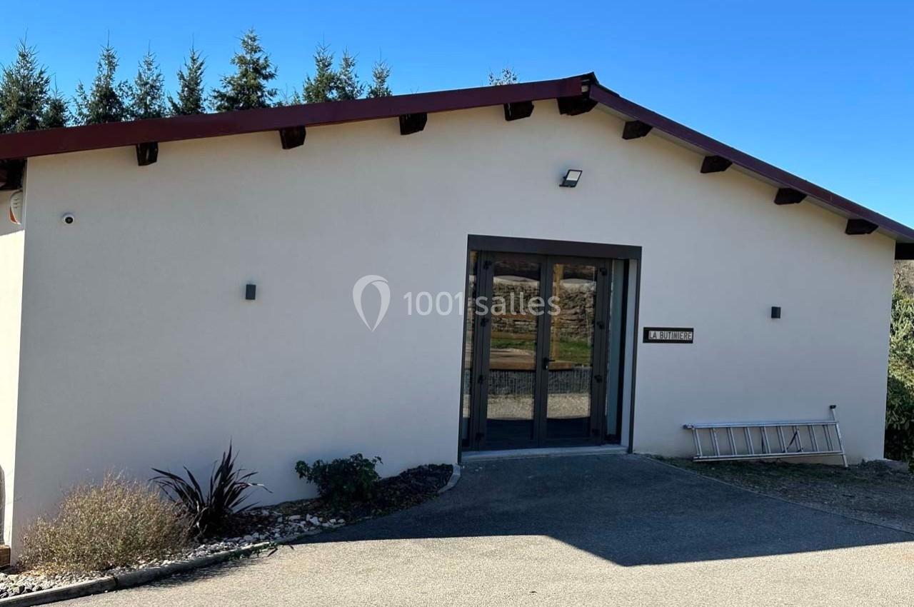 Façade d'un bâtiment beige avec une porte vitrée, une échelle posée au sol et des arbres en arrière-plan.