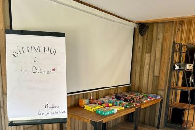 Des chèvres et des chevreaux devant une cabane en bois dans un enclos extérieur.