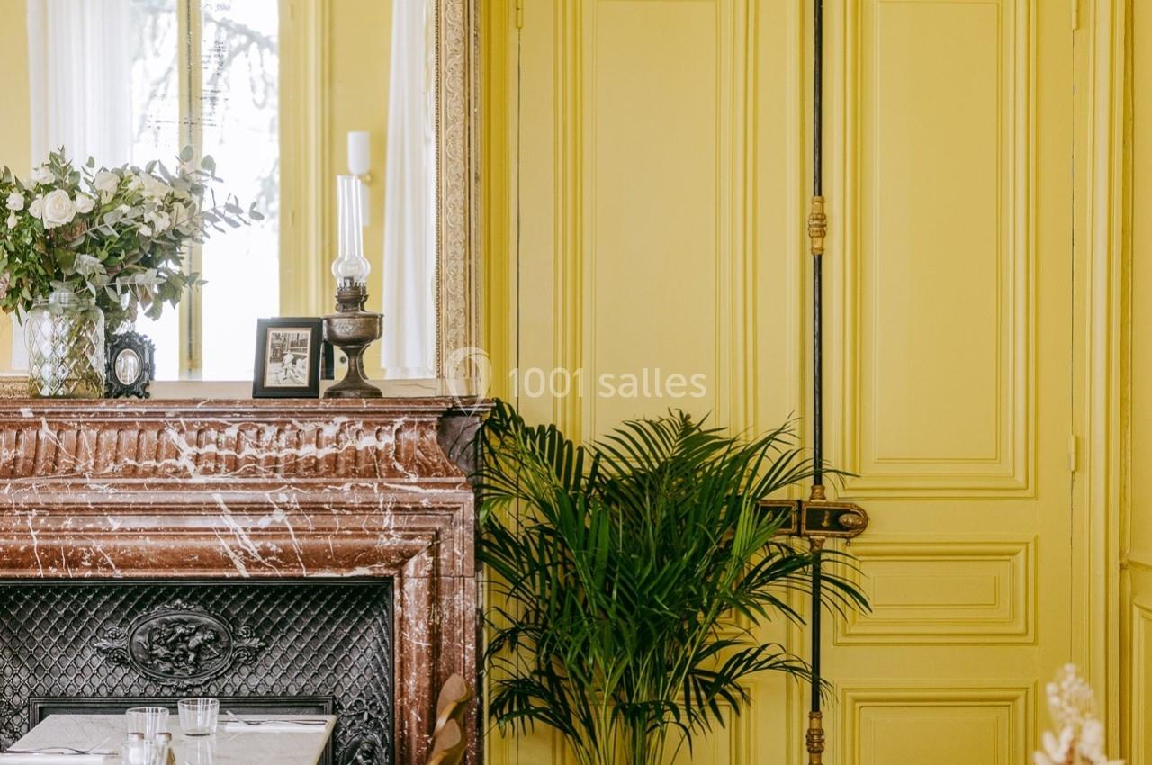 Salle à manger lumineuse avec murs jaunes, cheminée en marbre, miroir orné et table dressée pour deux.