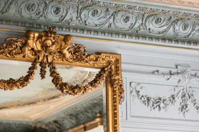 Façade d'une maison en briques avec toit mansardé, portail en fer forgé et arbres dénudés en premier plan.