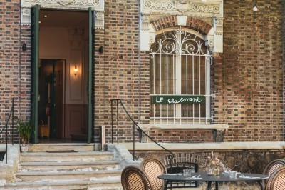 Façade d'une maison en briques avec toit mansardé, portail en fer forgé et arbres dénudés en premier plan.